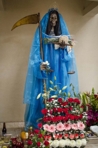 A Santa Morte é uma figura esquelética, vestida com um longo manto (um esqueleto sob um manto) e carregando um ou mais objetos, normalmente uma gadanha e um globo. 
