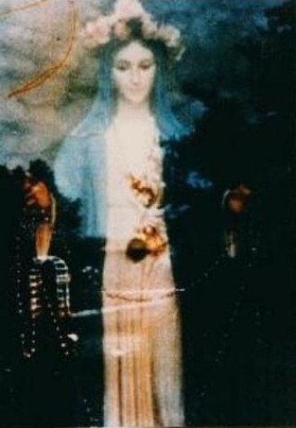 Em San Damiano (Itália), uma mulher fotografou a figura em frente ao portão, uma estátua de Maria. Esta maravilhosa Madonna surgiu quando a foto foi revelada. As linhas vermelhas no canto superior esquerdo simbolizam o cálice com a Santa Hóstia. 